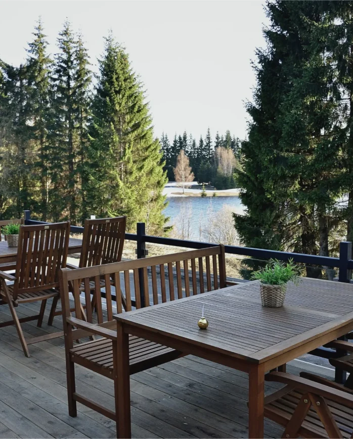 Venkovní dřevěná terasa Montanie Resort s posezením a výhledem přes smrkové lesy na přehradu Souš v Jizerských horách.