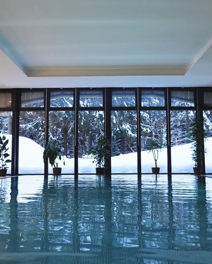 Krytý bazén ve wellness resortu Montanie s panoramatickými okny a výhledem na zasněžený smrkový les v Jizerských horách.